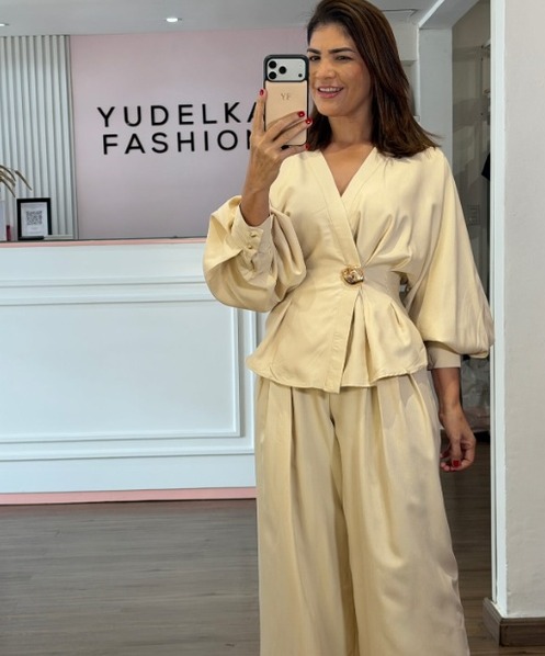 Clienta con un conjunto crema con cinturón frente al panel rosado de Yudelka Fashion
